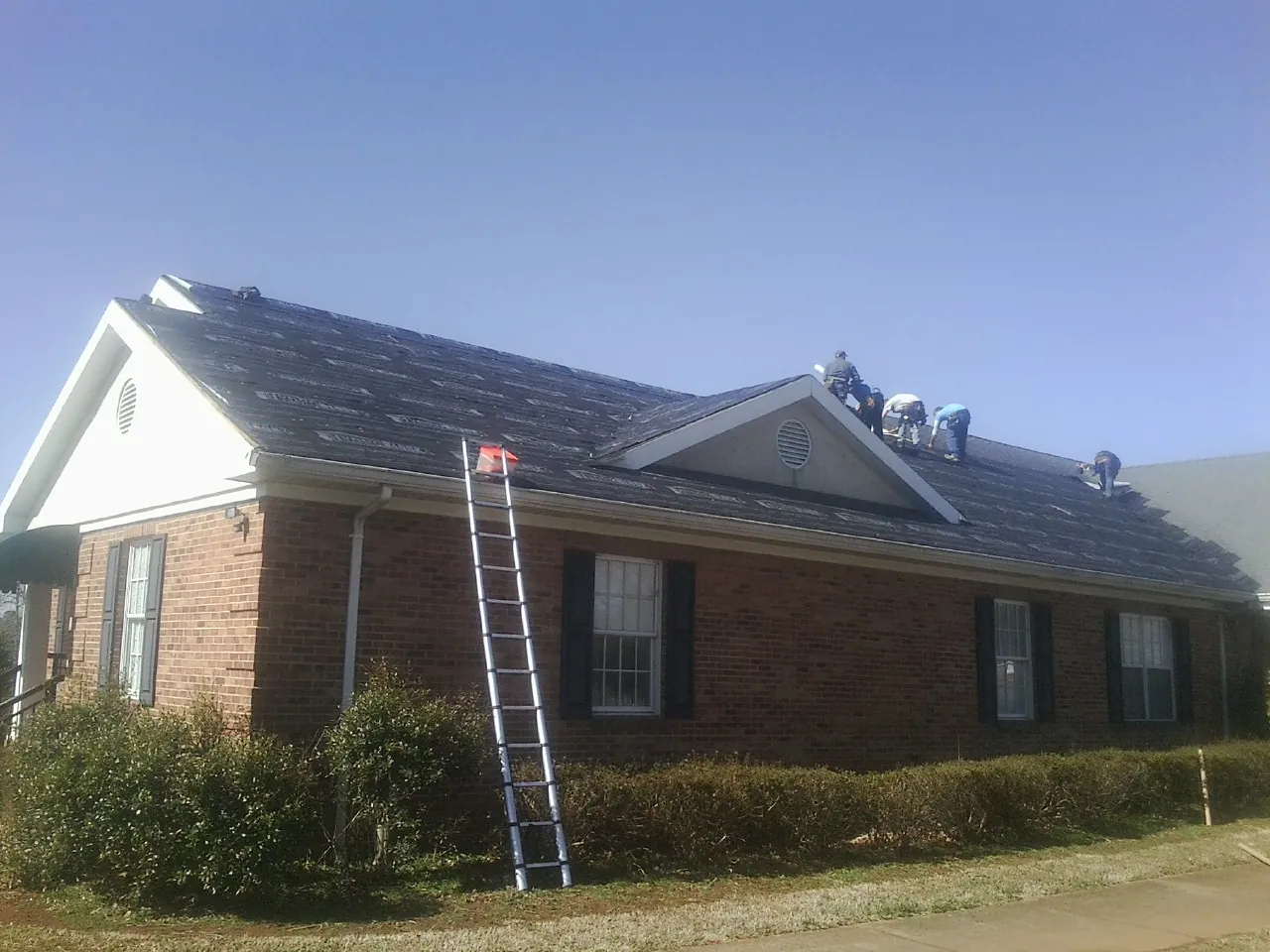 Crew tearing shingles off a brick ranch roof with a ladder set — Emergency Roof Repair work by our crew in Port Elizabeth